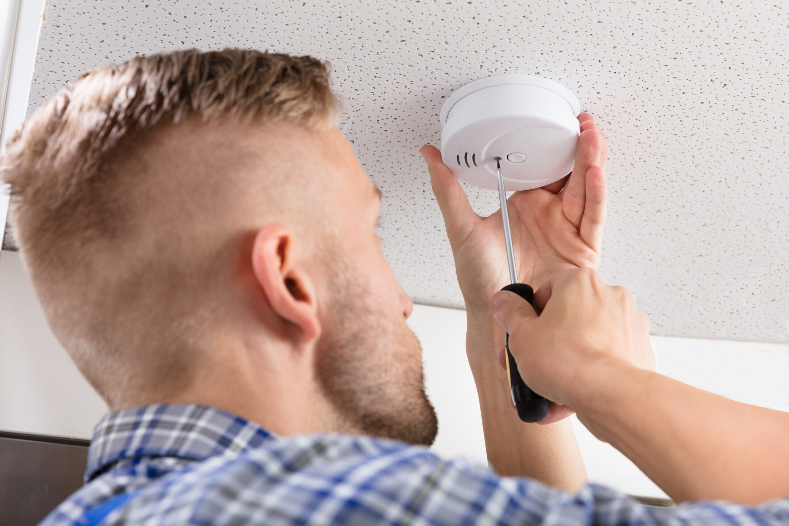 Close-up of a Person’s Hand Using Screwdriver to Install Smoke Detector on Ceiling at Home